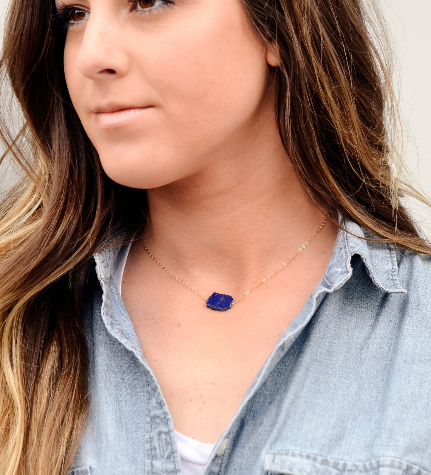 Natural blue lapis lazuli slice set onto a sterling silver chain. The stone is smooth polished with raw edges and oval in shape. Natural pyrite and calcite flecks are visible within each stone. Modeled image.