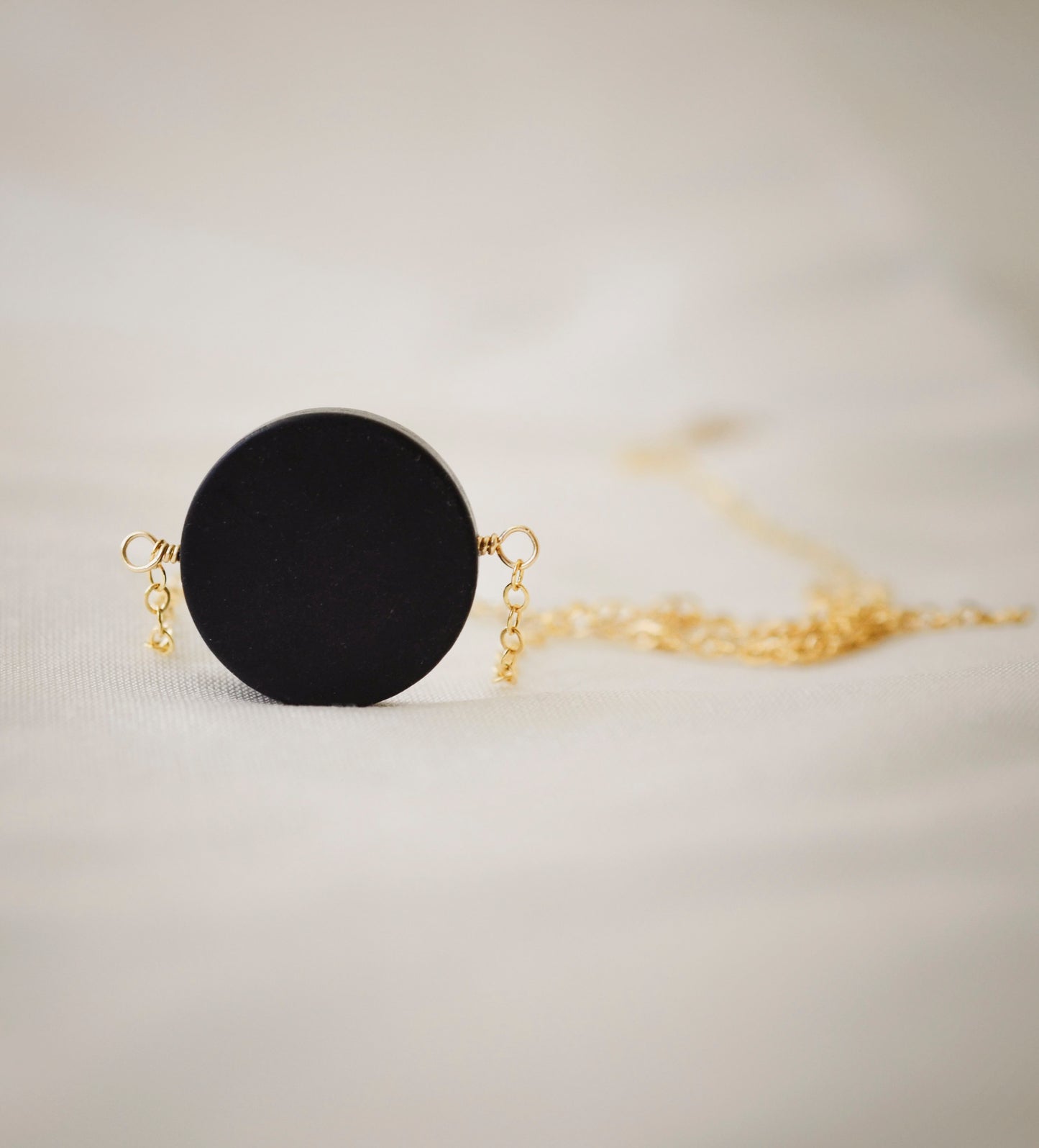 Matte black Onyx circle pendant suspended from a 14k gold filled chain. The stone has a smooth matte finish.