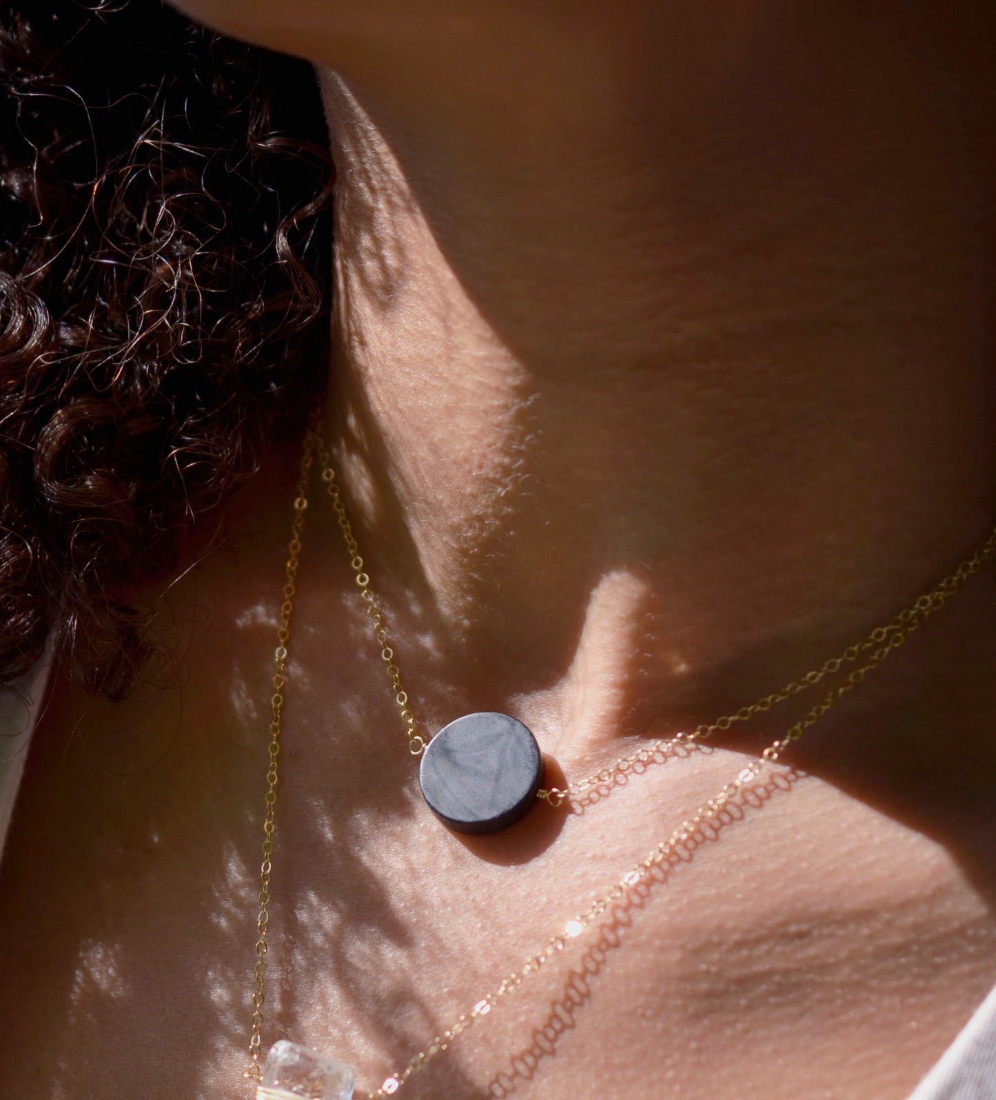 Matte black Onyx circle pendant suspended from a 14k gold filled chain. The stone has a smooth matte finish.