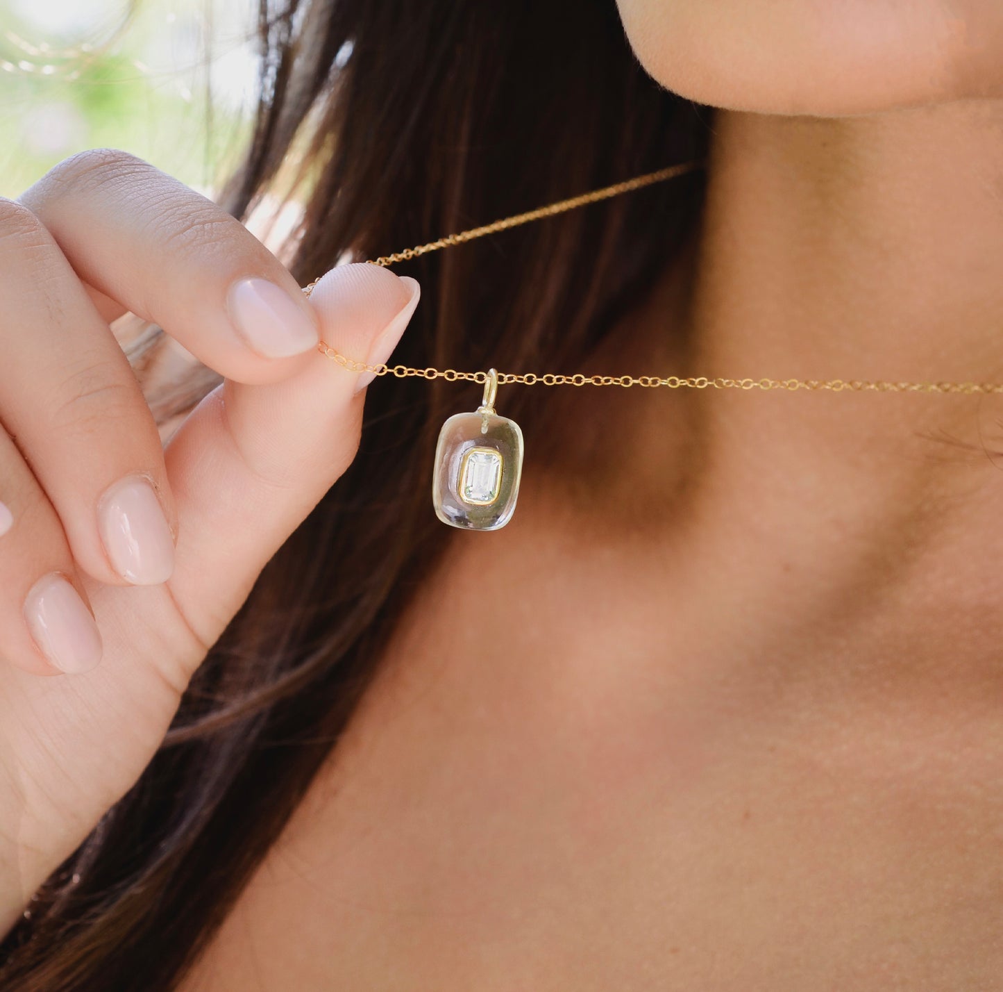 Close-up of a gold necklace with a clear pendant worn by a woman.
Handmade Maris necklace featuring a Blue Topaz set inside a clear Rock Crystal frame on a 14K Gold Filled chain. Ideal gift for wife, girlfriend, or mom. Minimalist topaz pendant for layering.