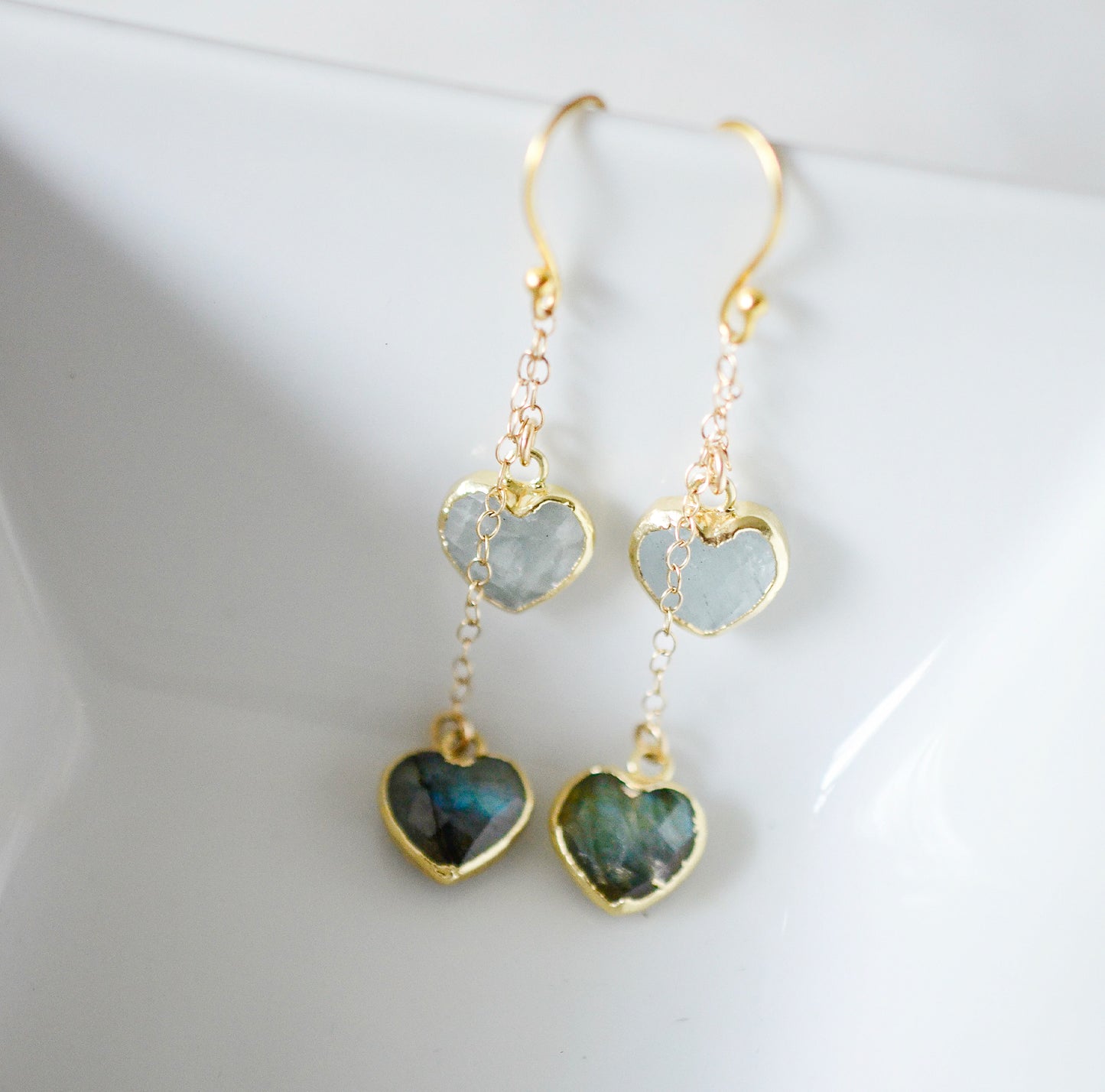 Close-up of heart dangle earrings. The gold gemstone dangle earrings feature aquamarine and labradorite hearts. They're a perfect romantic gift for her, wife, girlfriend, valentines day.