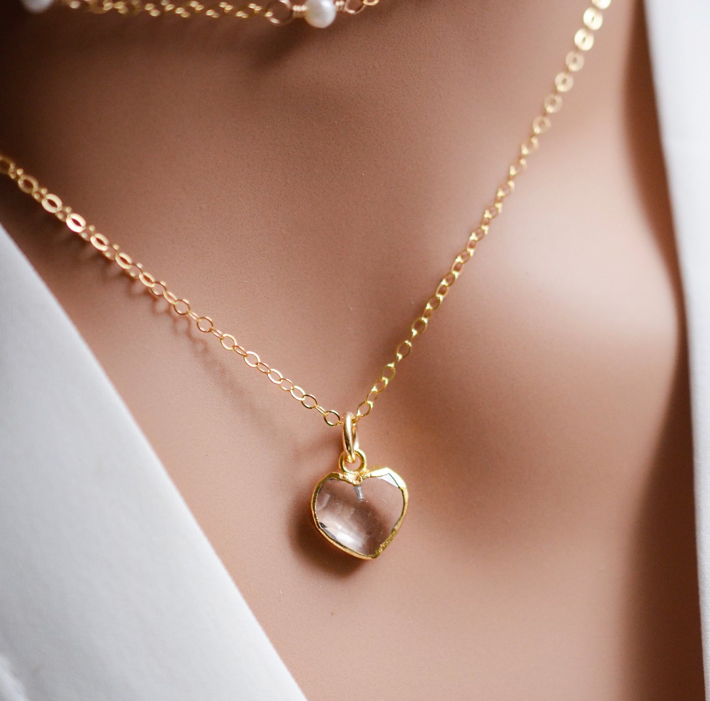 Close up image of a clear crystal quartz gemstone in a heart shape. The chain is 14k gold filled.