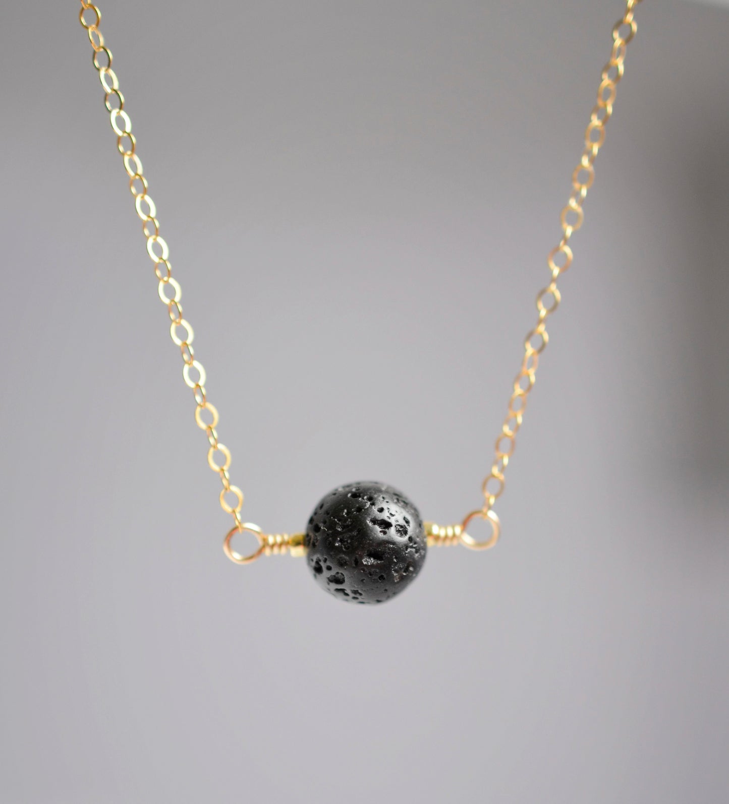 Close up of a natural black lava stone pendant on a gold filled chain.