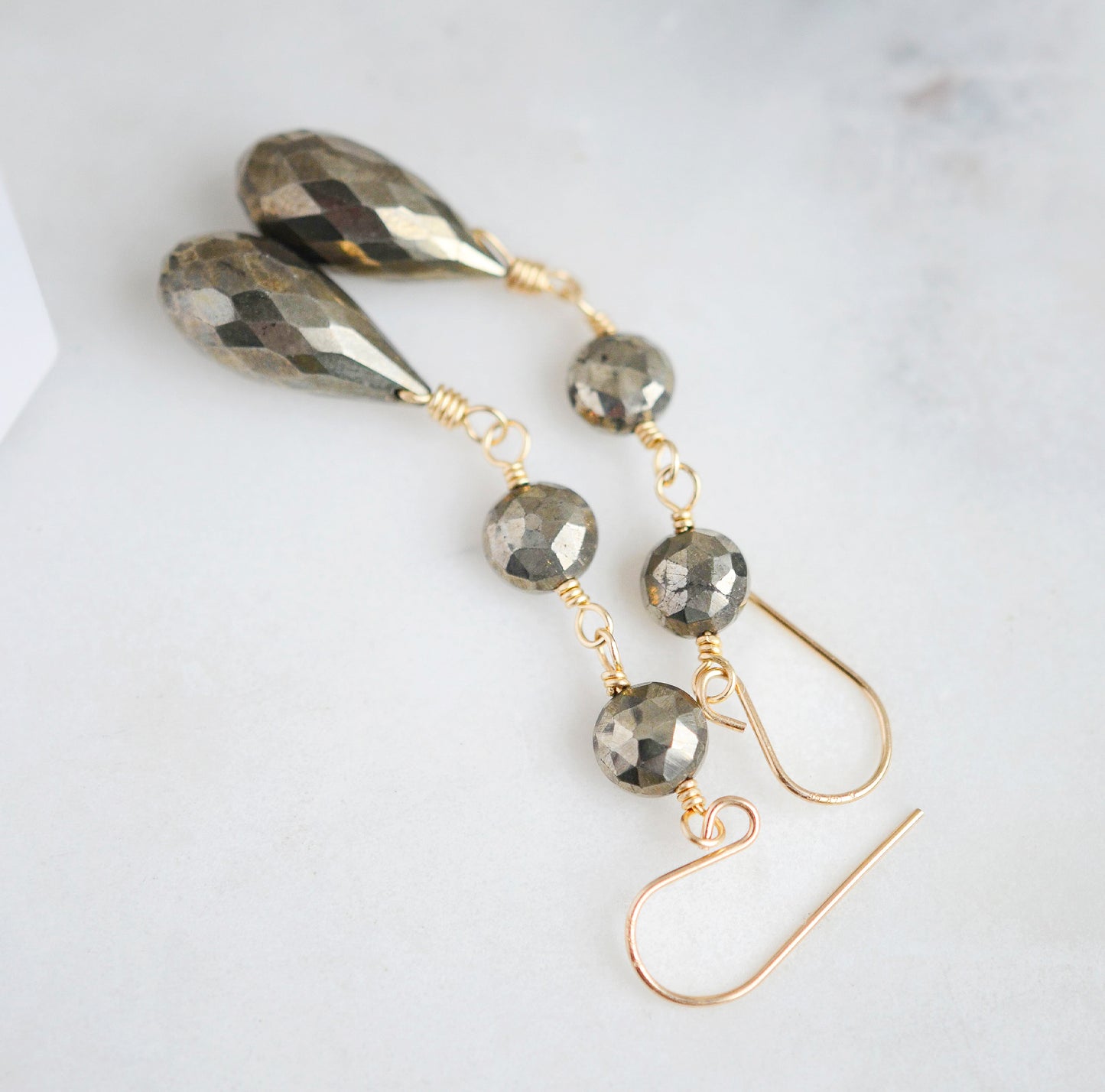 Close up of faceted pyrite coin gemstones. Long teardrop earrings shown in 14k gold filled.
