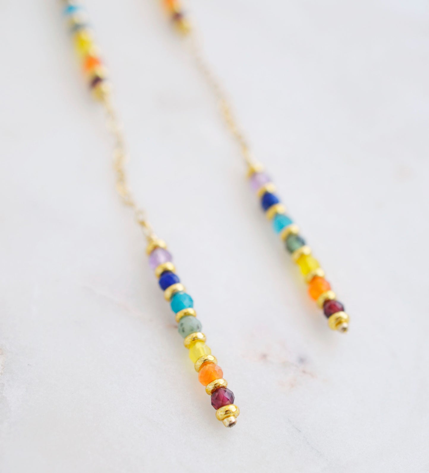 Close up. Two long, straight bars of crystals arranged in a rainbow pattern separated by a dainty chain. The gold style is shown.