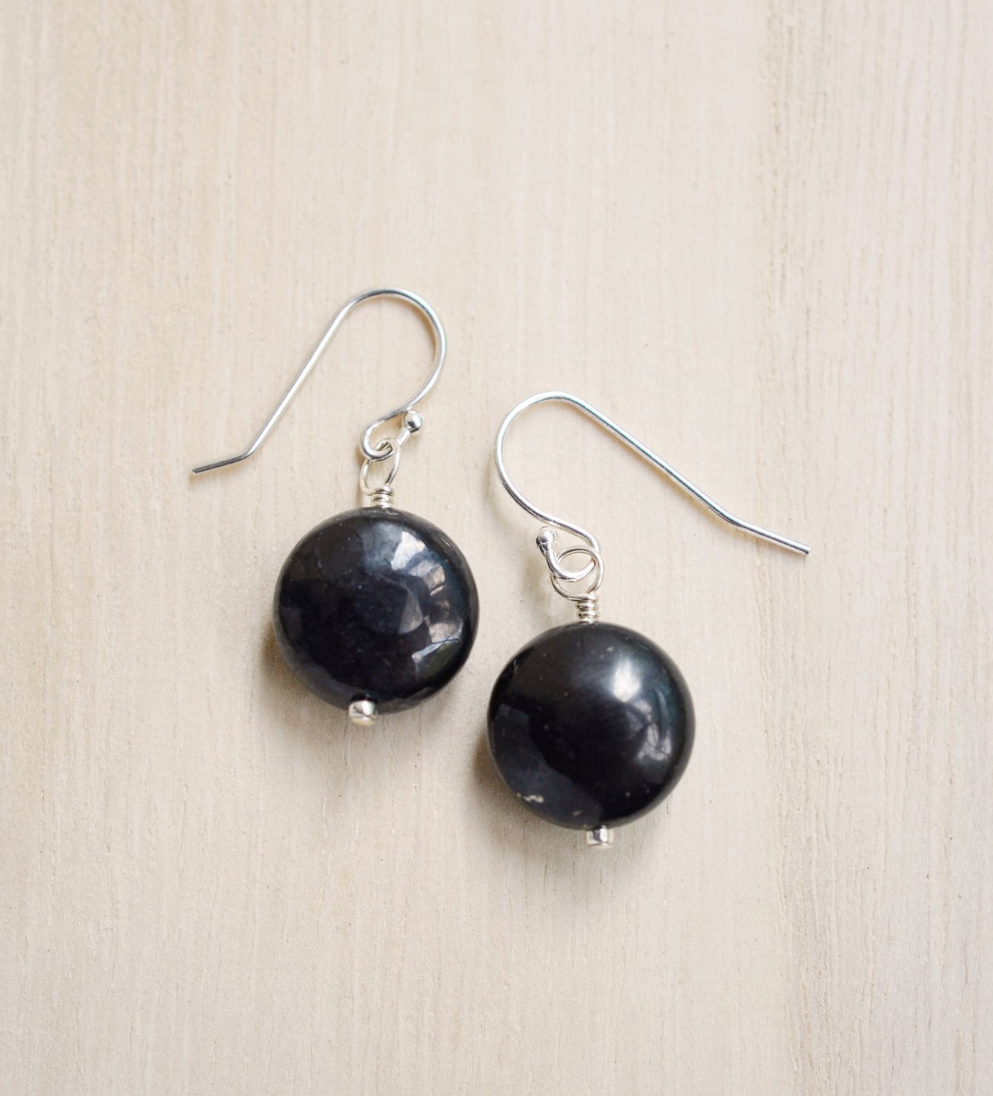 Natural smooth polished coin shape black Shungite dangle from sterling silver earring hooks.
