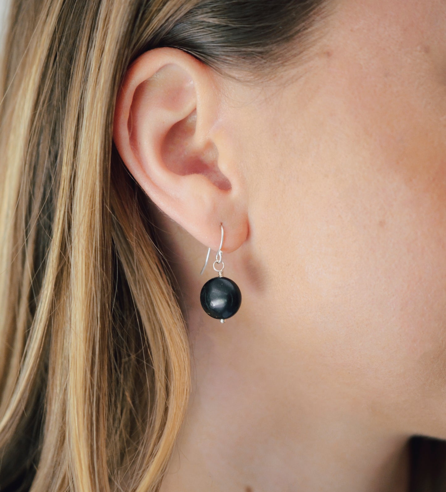 Natural smooth polished coin shape black Shungite dangle from sterling silver earring hooks. Modeled image.
