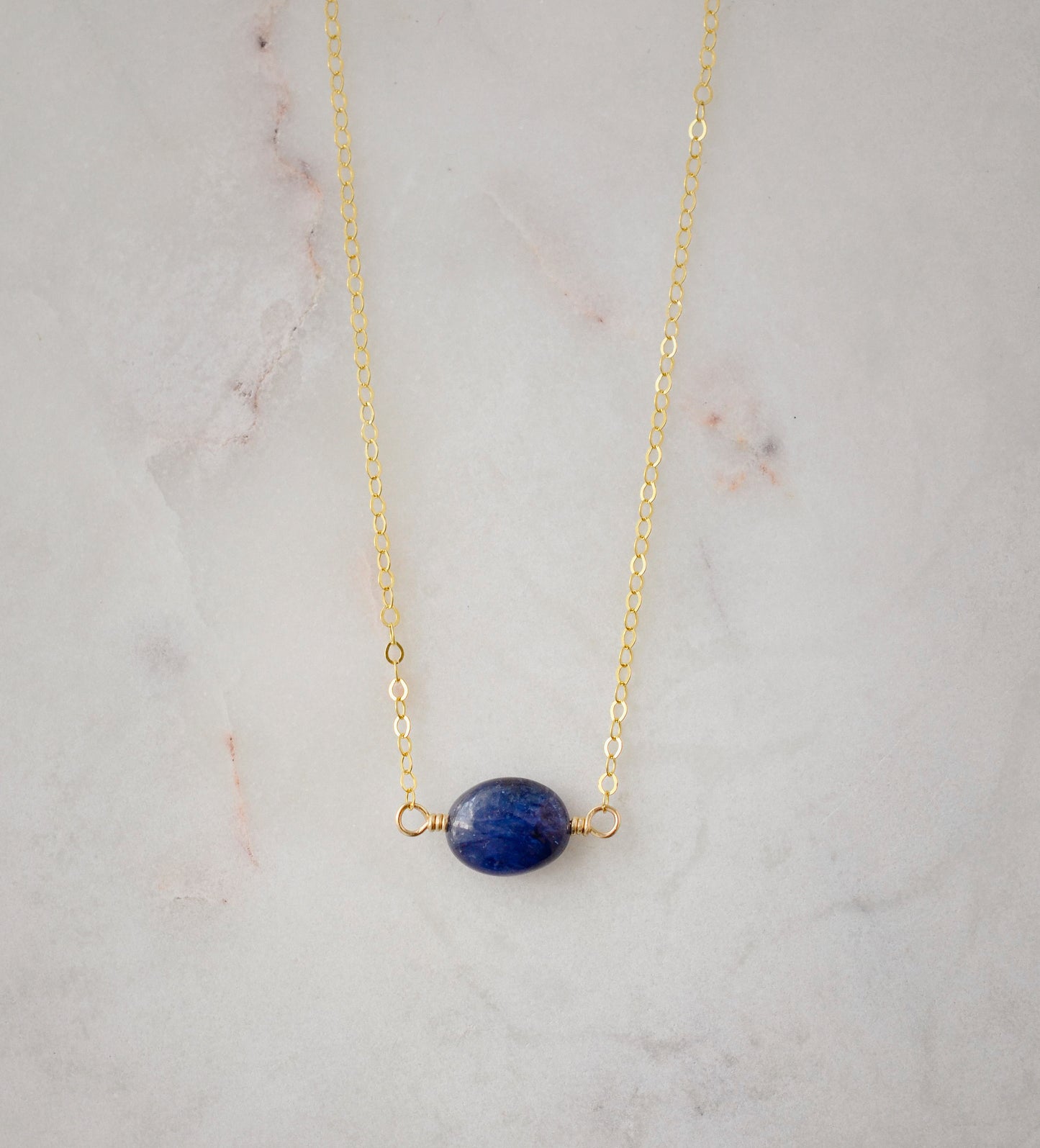 Small blue sapphire stone set onto a gold chain. The stone is a puffed oval shape.