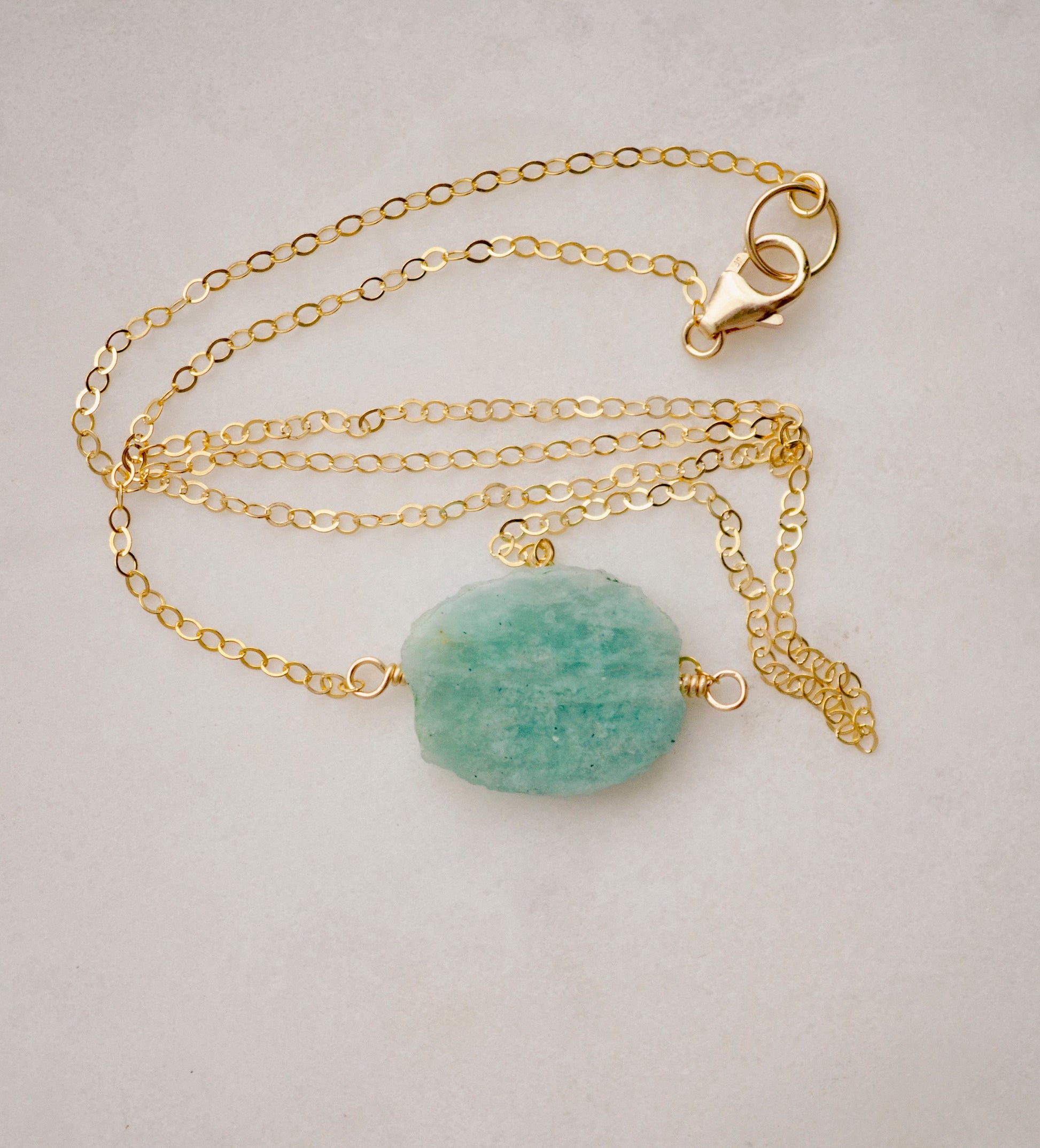 Aqua blue amazonite slice gemstone set onto a 14k gold filled chain. The stone is semi oval in shape, but irregular. It's smooth polished, but with raw edges. Shown with non-adjustable length clasp.