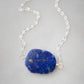 Natural blue lapis lazuli slice set onto a sterling silver chain. The stone is smooth polished with raw edges and oval in shape. Natural pyrite and calcite flecks are visible within each stone. 