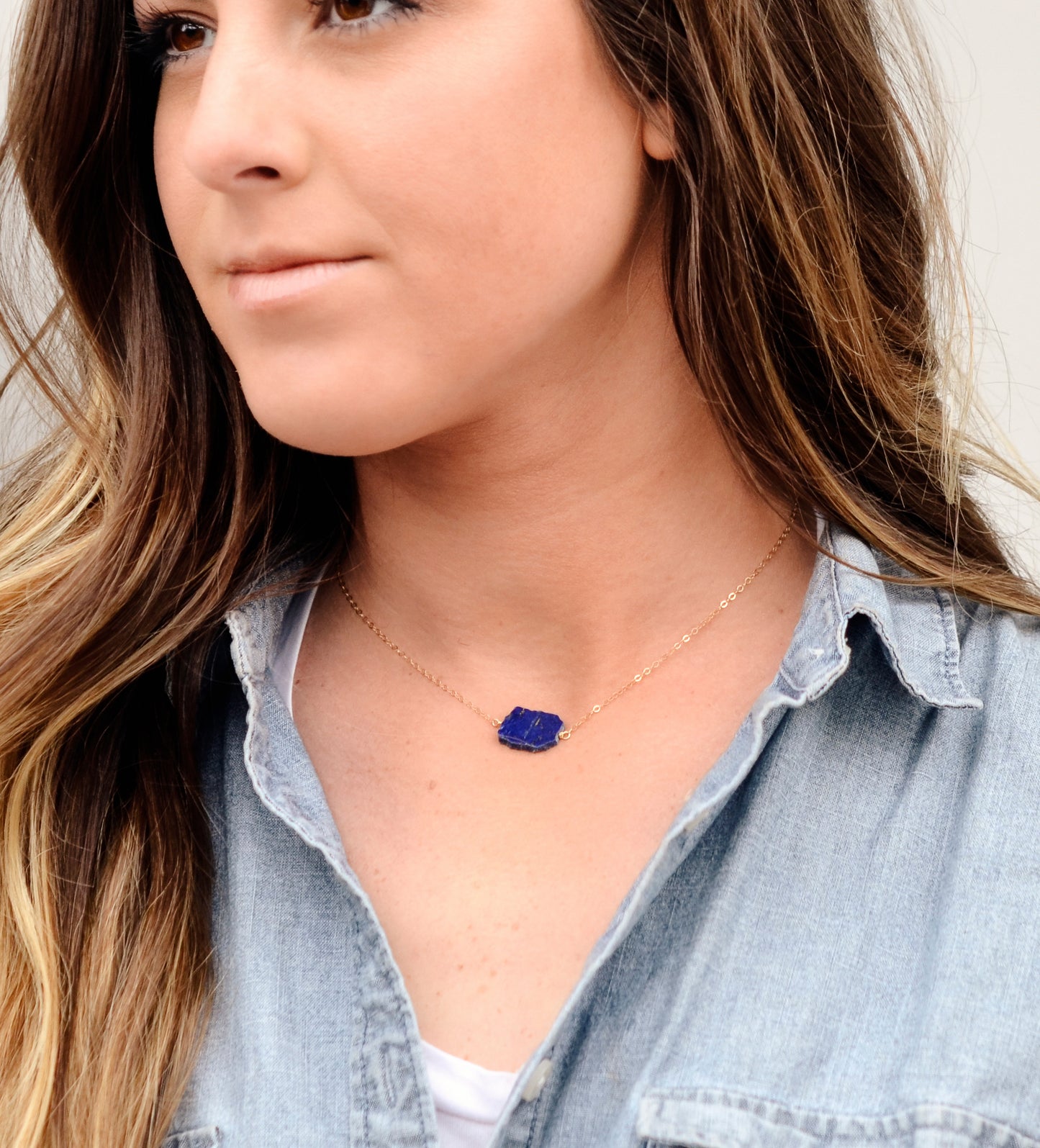 Natural blue lapis lazuli slice set onto a sterling silver chain. The stone is smooth polished with raw edges and oval in shape. Natural pyrite and calcite flecks are visible within each stone.  Modeled image.