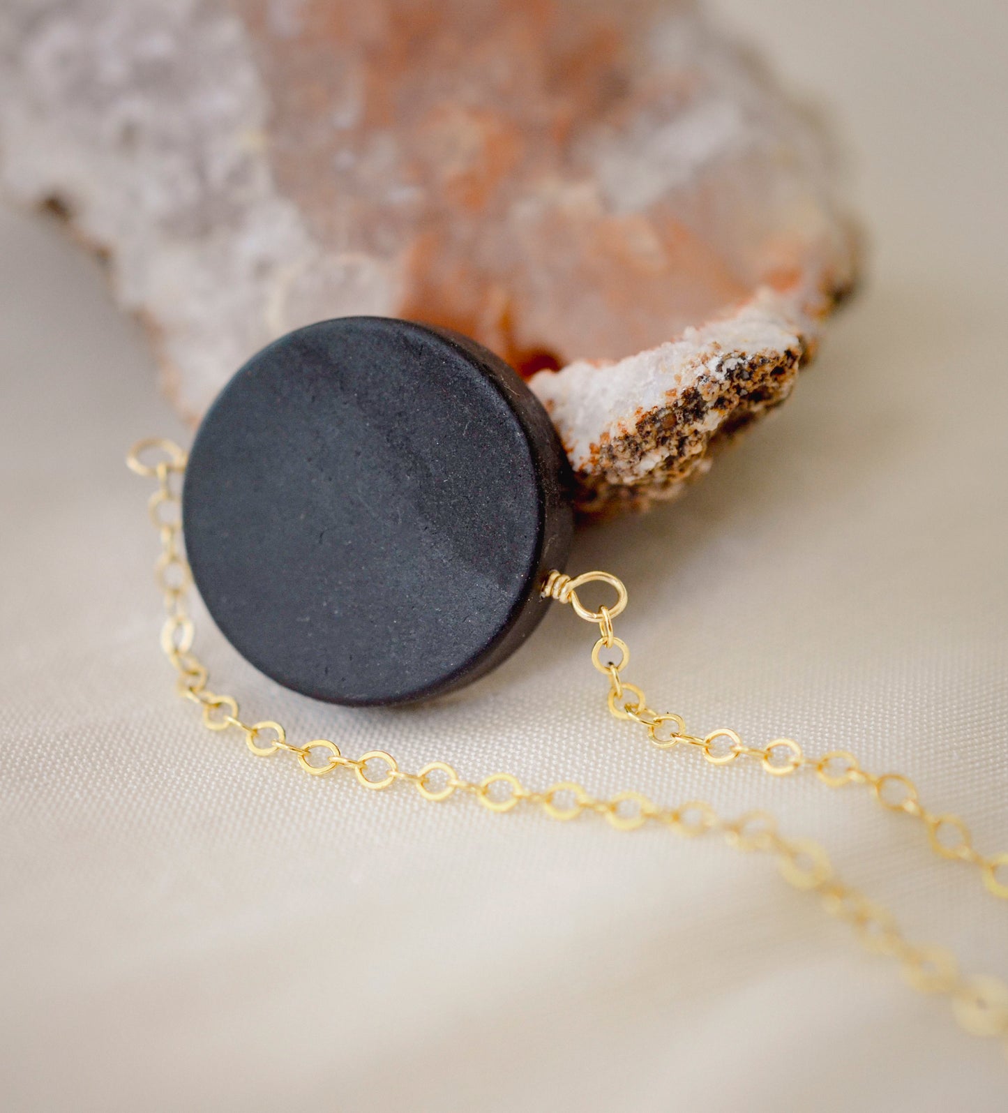 Matte black Onyx circle pendant suspended from a 14k gold filled chain. The stone has a smooth matte finish. 