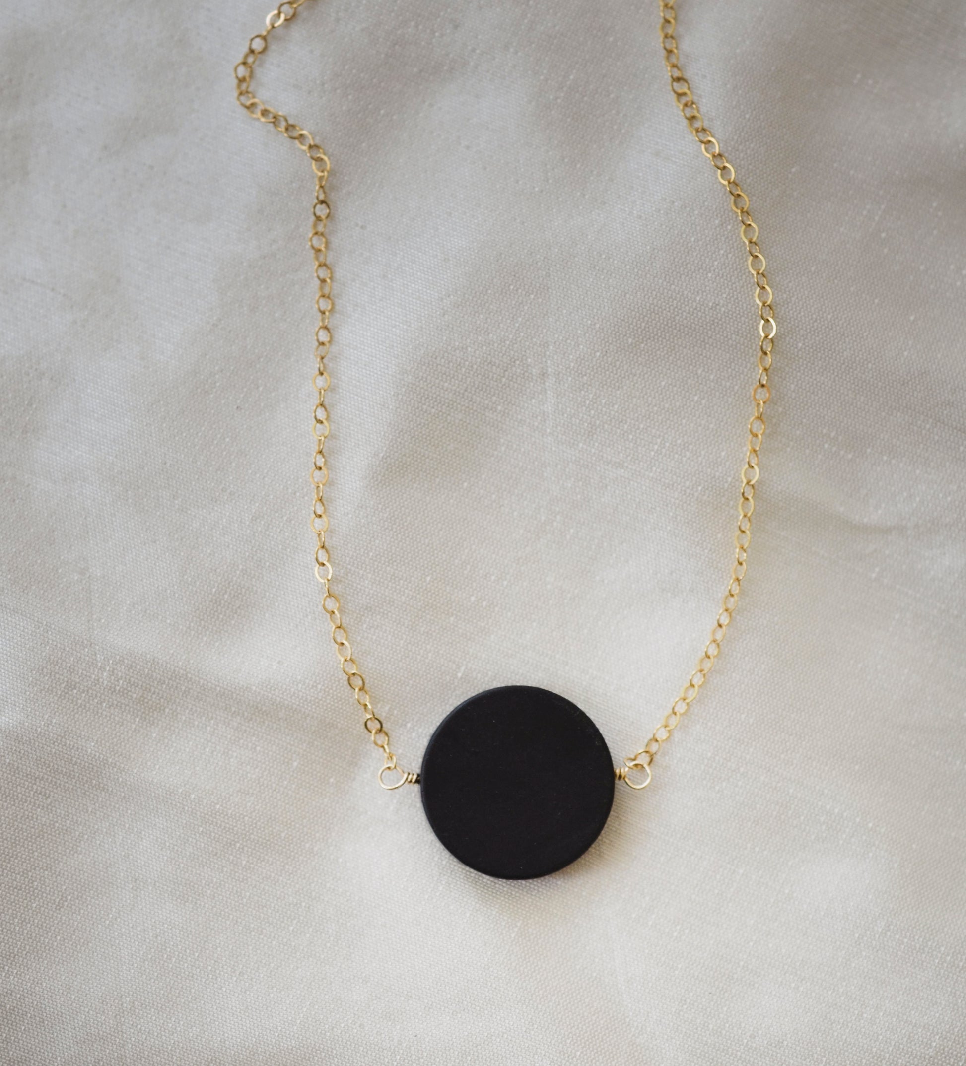 Matte black Onyx circle pendant suspended from a 14k gold filled chain. The stone has a smooth matte finish. 