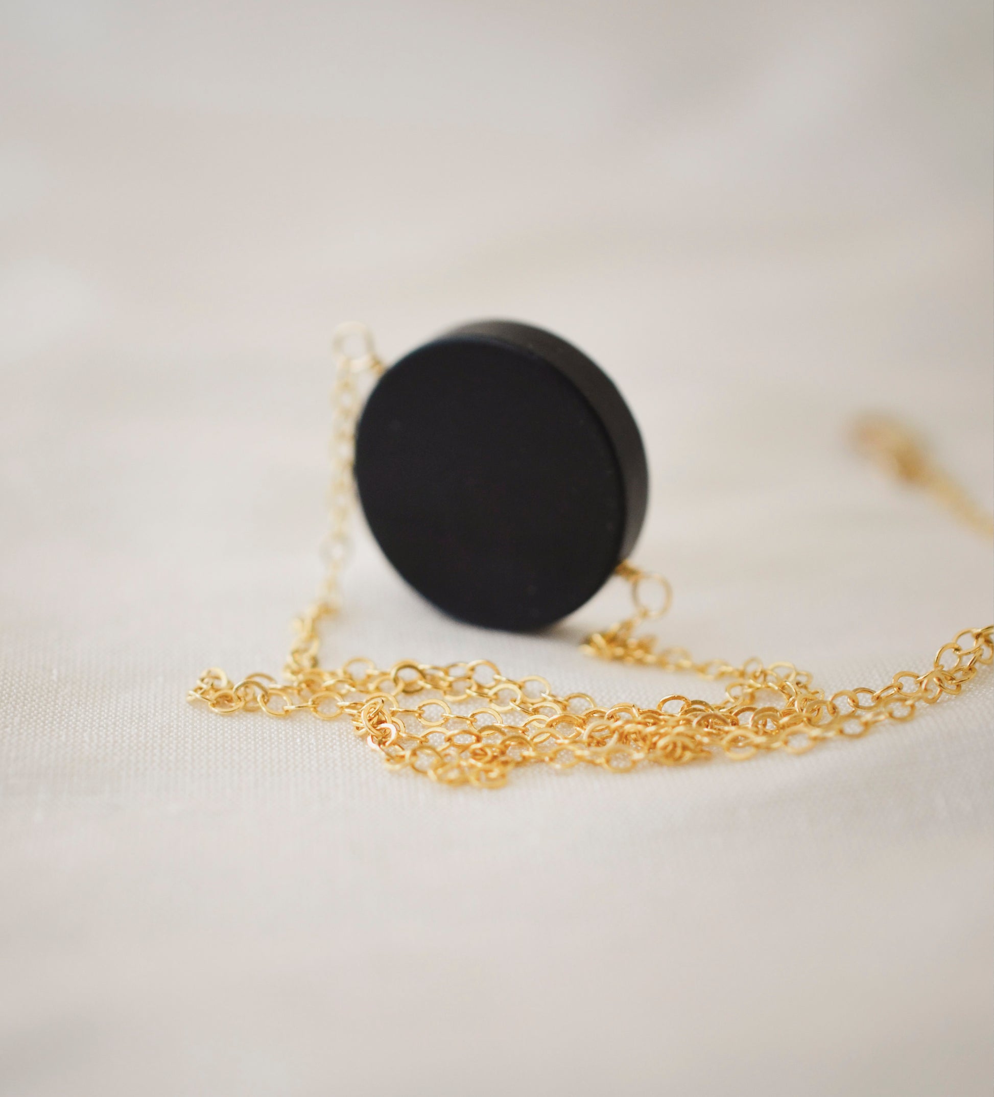 Matte black Onyx circle pendant suspended from a 14k gold filled chain. The stone has a smooth matte finish. 