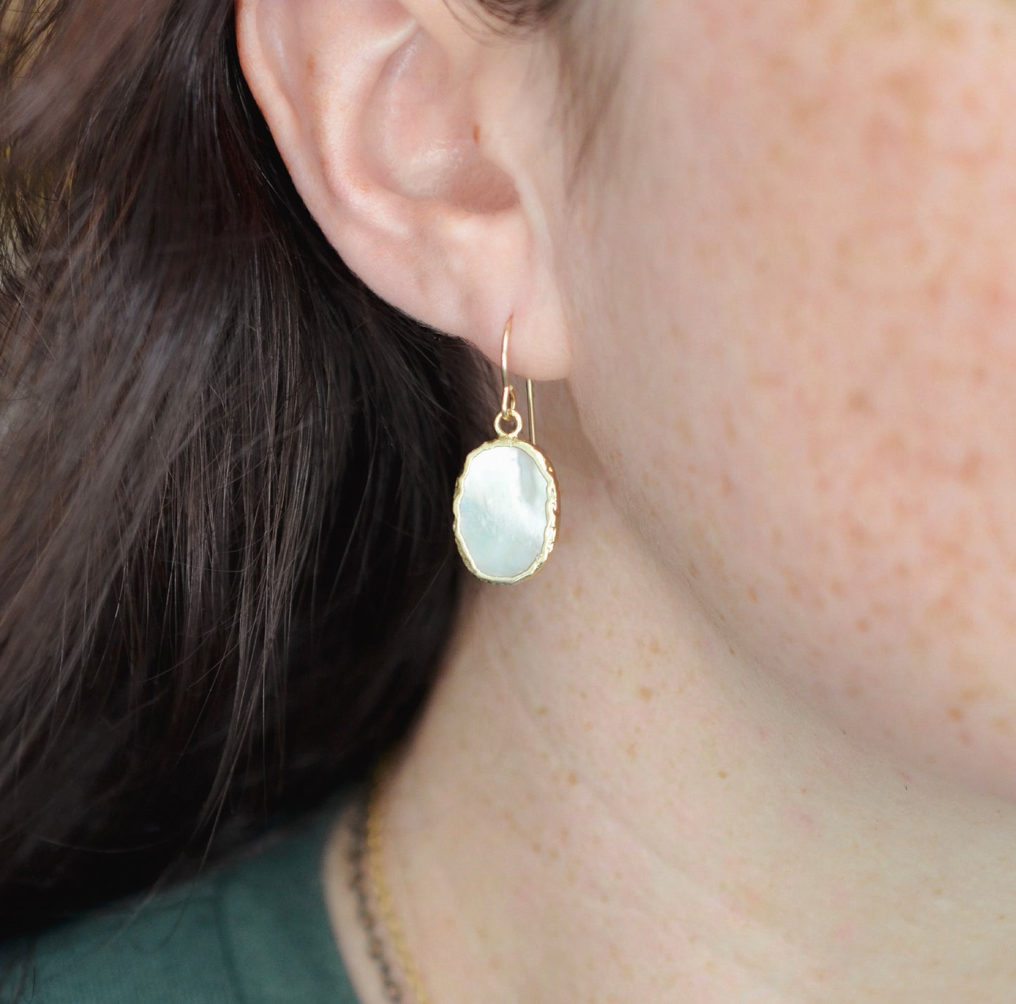 Modeled image. These handmade white mother of pearl earrings are edged in gold and set on 14k gold filled earring hooks. This dainty minimalist style is perfect for everyday, but also classic enough for weddings and bridesmaids.