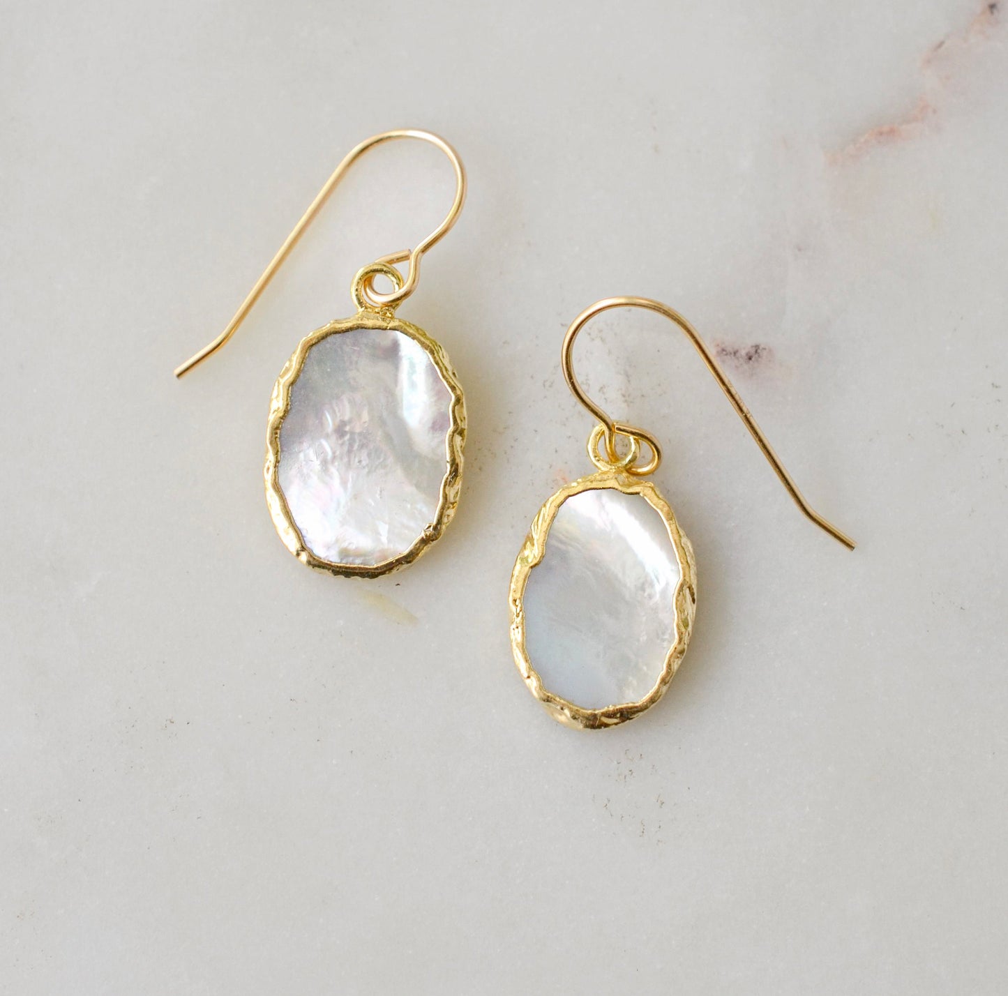 A pair of natural oval mother of pearl earrings dipped in 24k gold and set on 14k gold filled earwires. The shells are smooth polished and flash shades of white and silver.