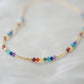 Tiny stones arranged in the order of the seven chakras or rainbow colors. Colors include: purple, blue, aqua, green, yellow, orange, and red. Close up of the gold style.
