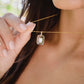 Close-up of a gold necklace with a clear pendant worn by a woman. 
Handmade Maris necklace featuring a Blue Topaz set inside a clear Rock Crystal frame on a 14K Gold Filled chain. Ideal gift for wife, girlfriend, or mom. Minimalist topaz pendant for layering.