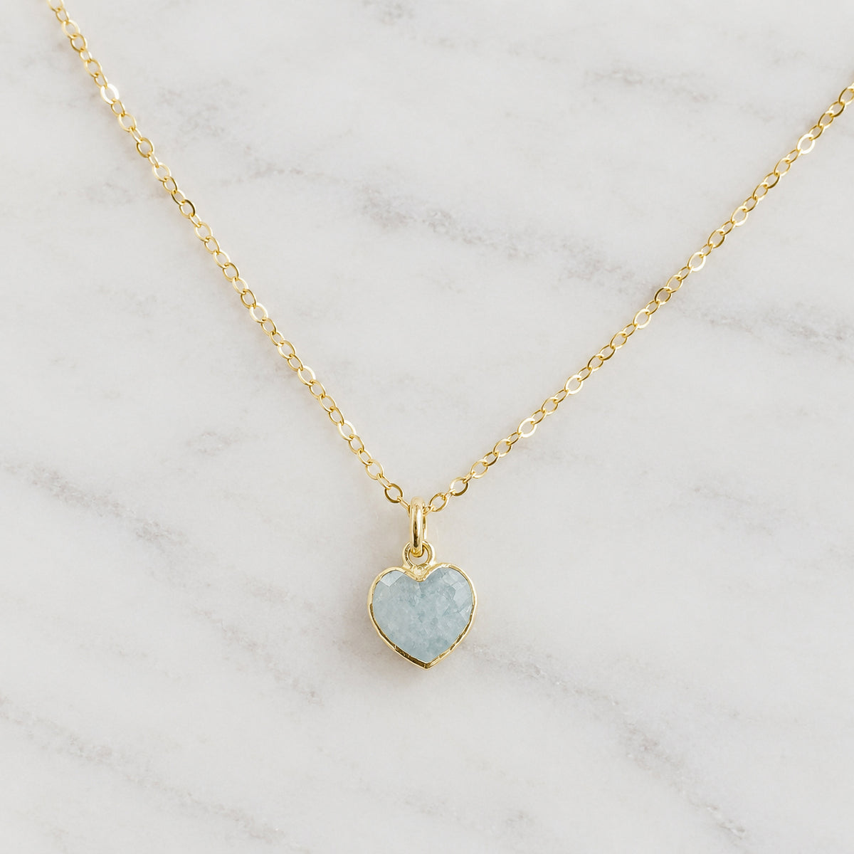 A delicate 14k gold-filled chain necklace with a small heart-shaped pendant featuring a light blue, natural aquamarine stone. Handmade in Connecticut by Gemnia.