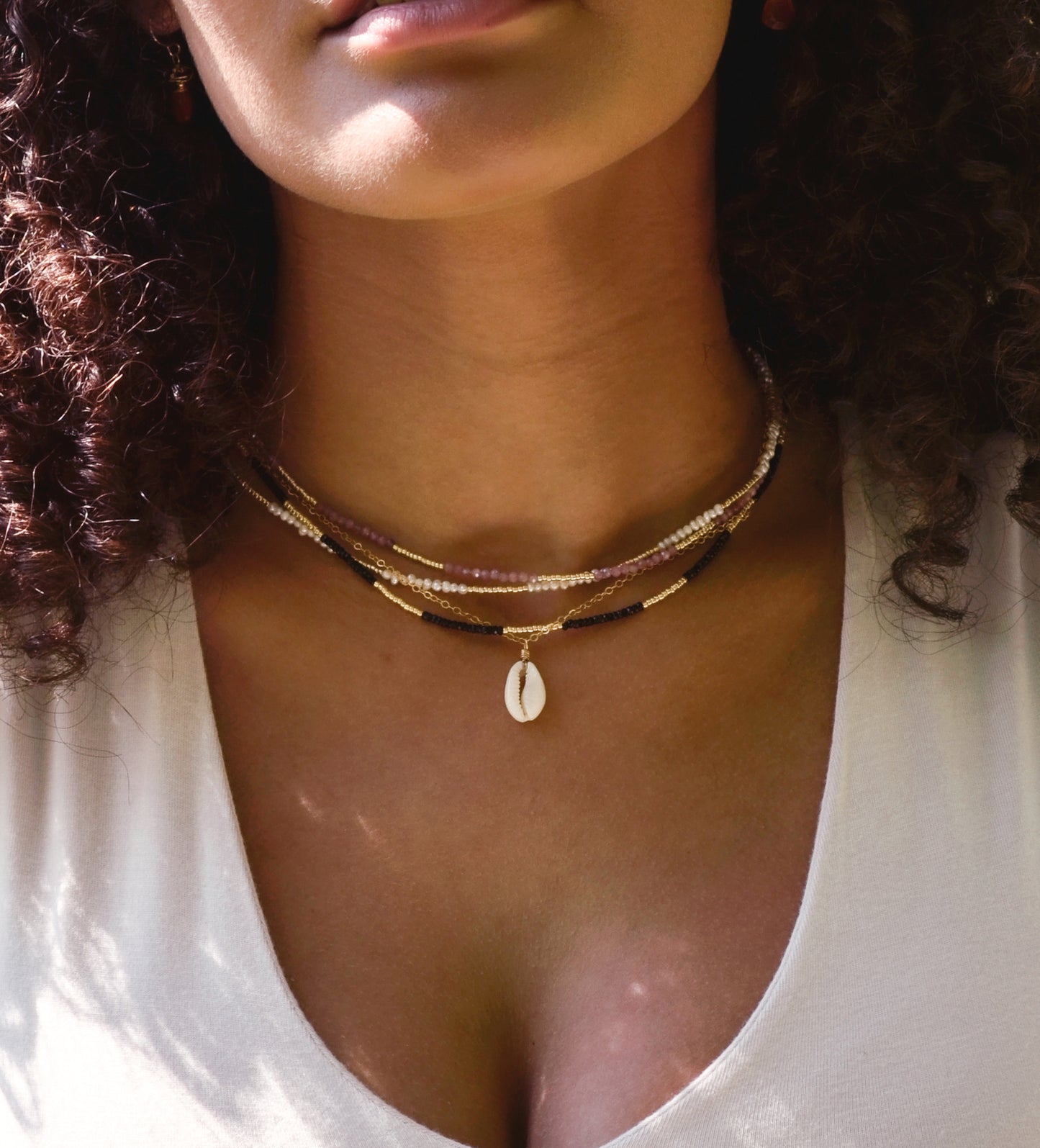 Single cowrie shell suspended from a 14k gold filled chain necklace. Modeled with other beaded crystal necklaces.