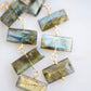 Close up image: Four faceted emerald cut labradorite gemstones dangle in these 14k gold filled earrings. Each stone flashes blue or green.