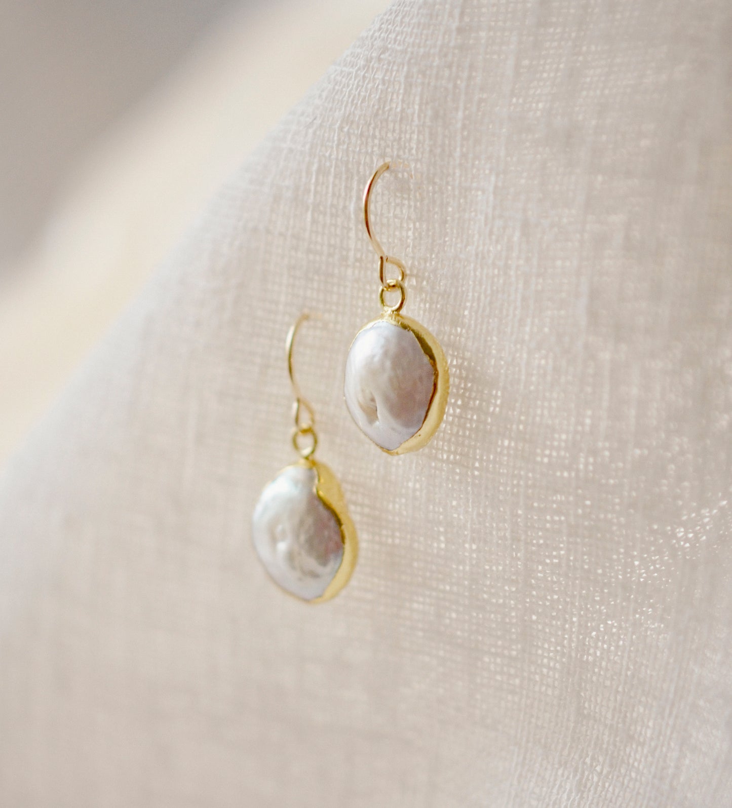 Side view. Natural white freshwater pearl dangle earring. The pearl is set in 22k gold electroplate and suspended from 14k gold filled earwires.