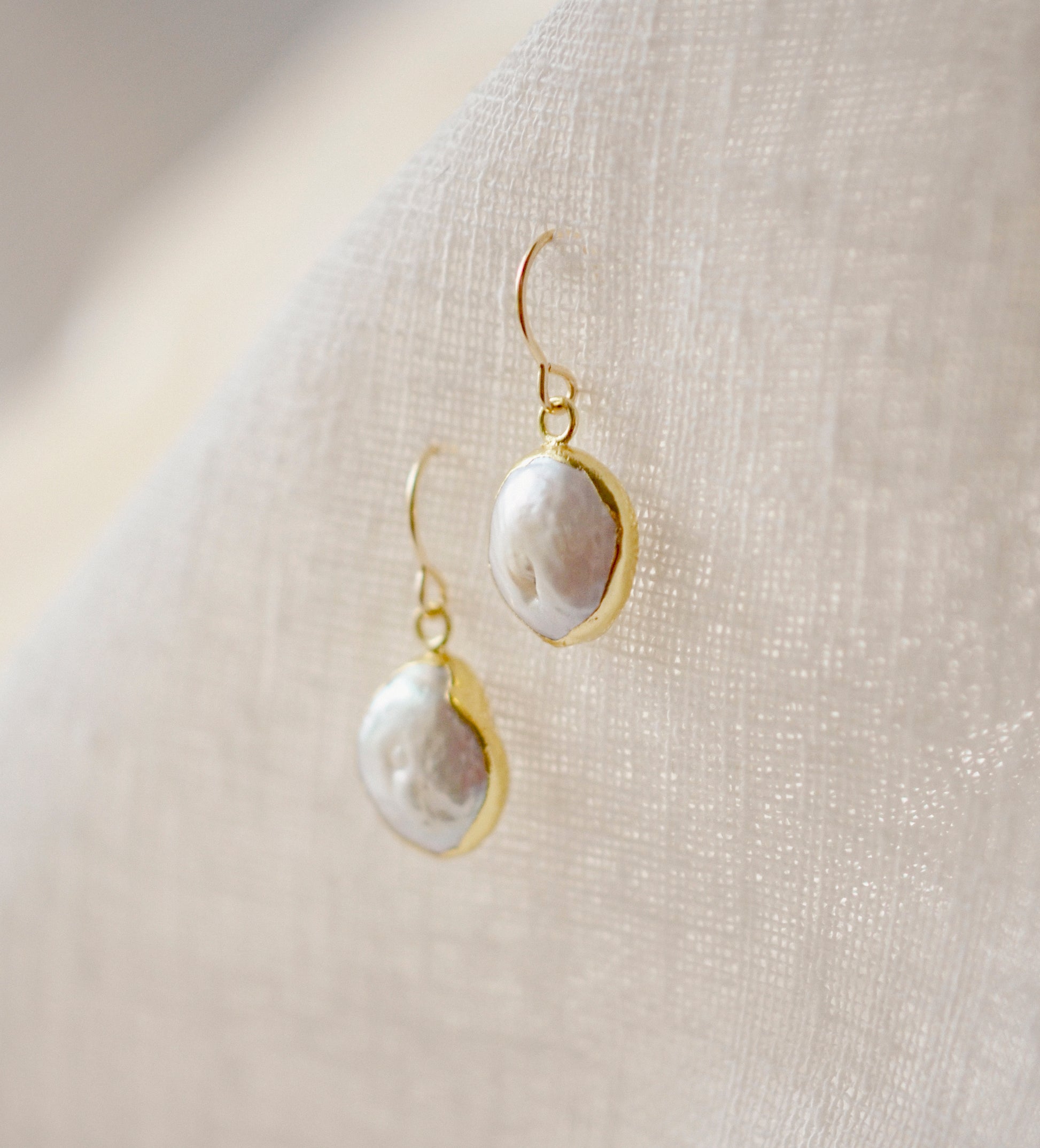 Side view. Natural white freshwater pearl dangle earring. The pearl is set in 22k gold electroplate and suspended from 14k gold filled earwires.