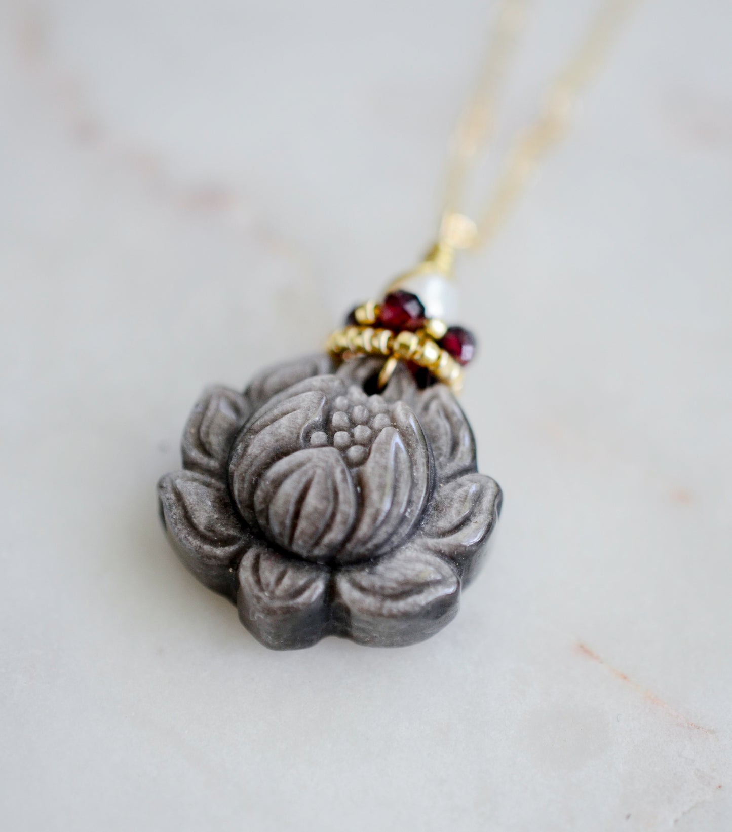Obsidian Lotus flower pendant on a chain with beads against a light background