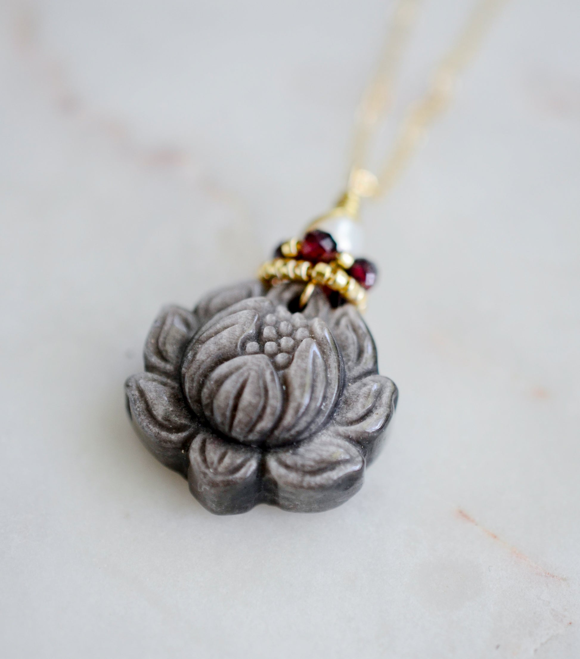 Obsidian Lotus flower pendant on a chain with beads against a light background