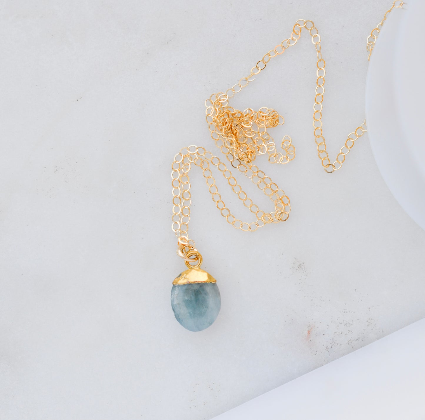 A handmade crystal necklace with a blue aquamarine teardrop pendant on a minimalist 14k gold filled chain. 