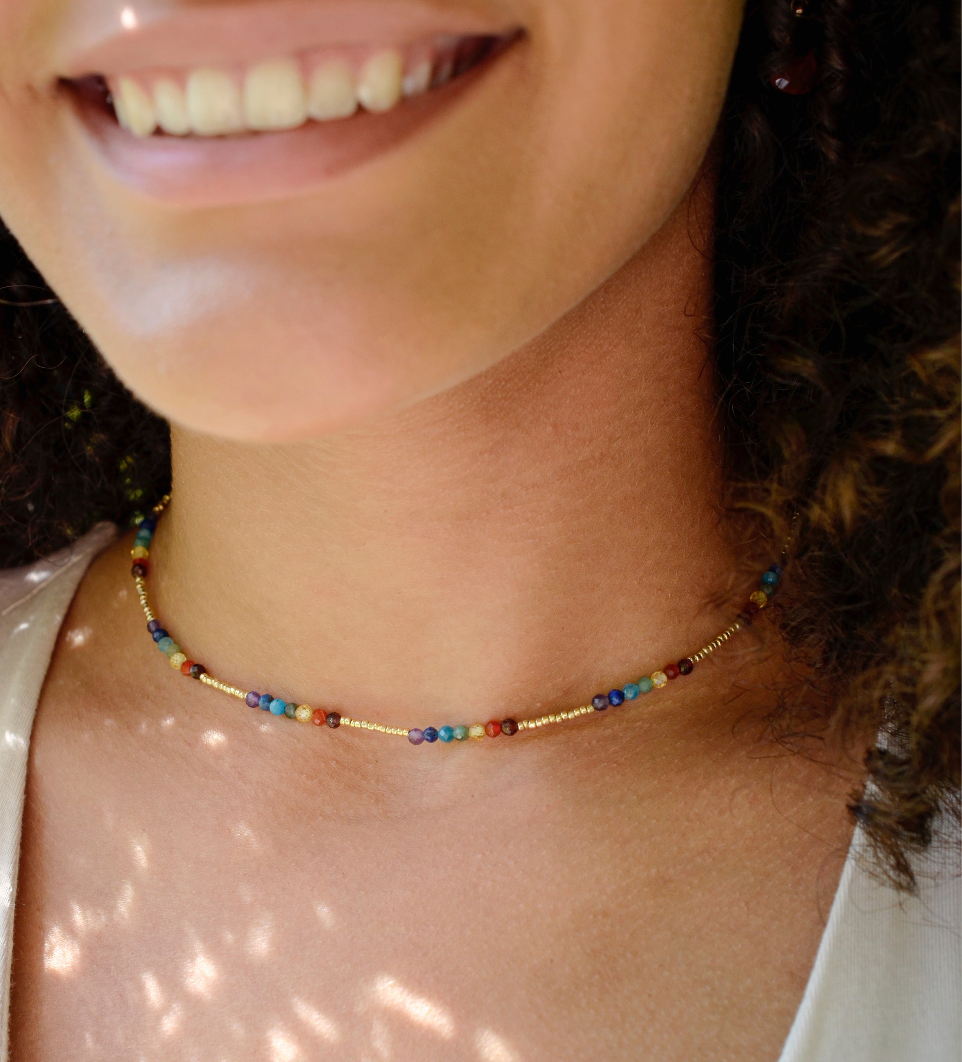 Tiny stones arranged in the order of the seven chakras or rainbow colors. Colors include: purple, blue, aqua, green, yellow, orange, and red. Modeled image. Handmade in Connecticut by Gemnia Jewelry.