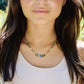 A woman wearing a beaded labradorite and white freshwater pearl necklace with five teardrops at the center. Shown in gold. 