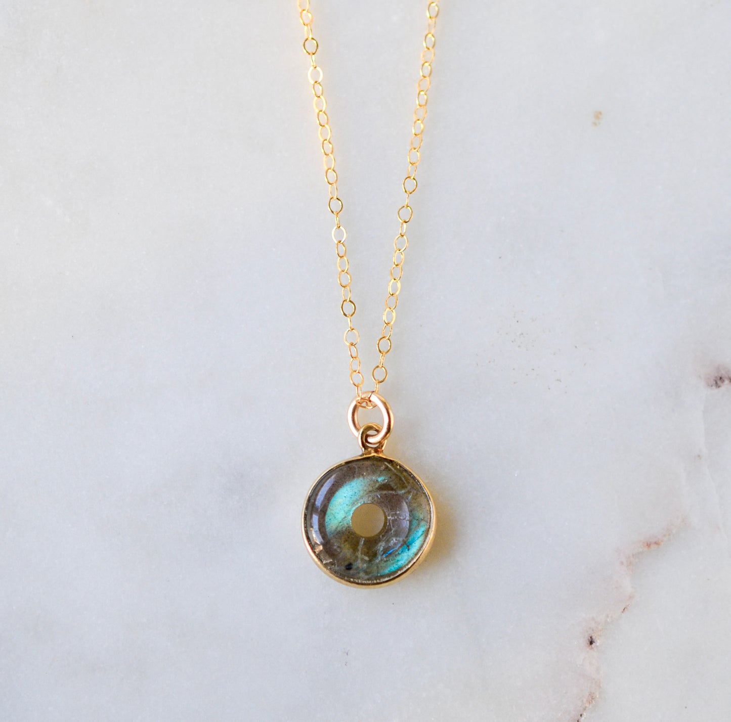 A doughnut shaped natural labradorite round pendant set in gold. The dainty chain is 14k gold filled. The jewelry is handmade in Connecticut by GEMNIA.