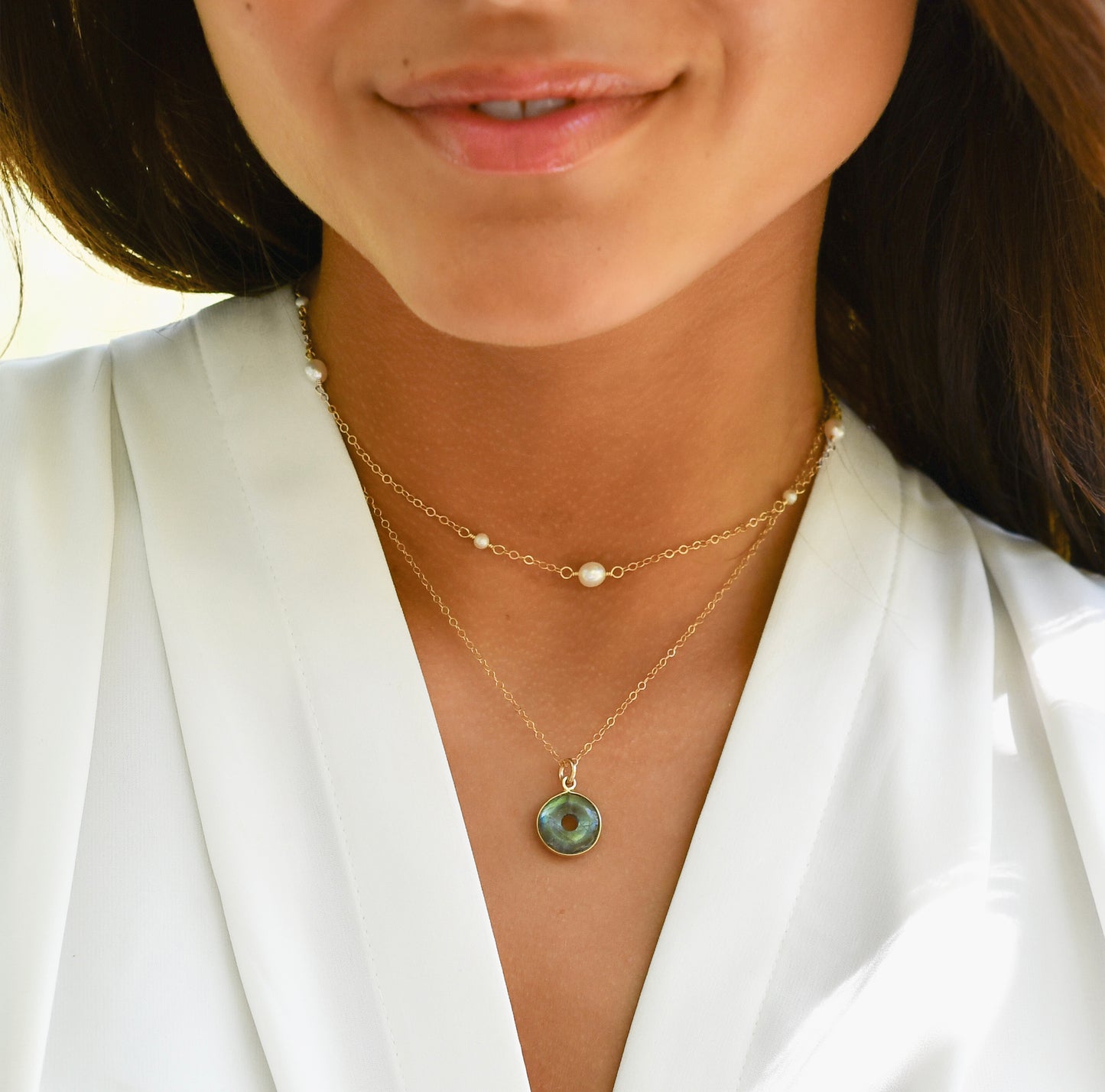 Close-up of a woman wearing a handcrafted artisan gold labradorite donut necklace with white freshwater pearl necklace chain. 