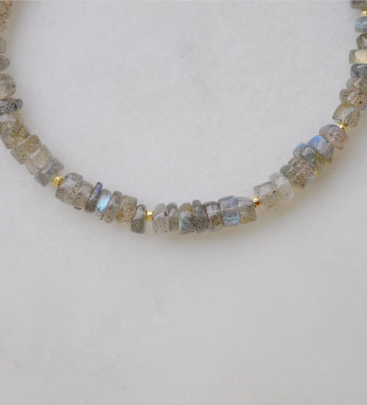 Blue flashing natural heishi or wheel shaped Labradorite gemstones strung together onto a bracelet. Tiny gold beads act as spacers between the stones. The gold style is shown.