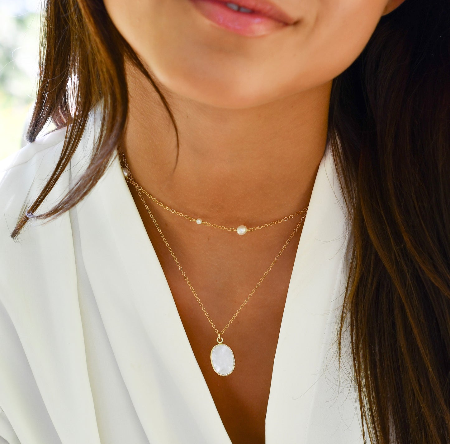Modeled image of a woman wearing two handmade, layered necklaces of genuine white freshwater pearls and natural mother of pearl in 14k gold filled.