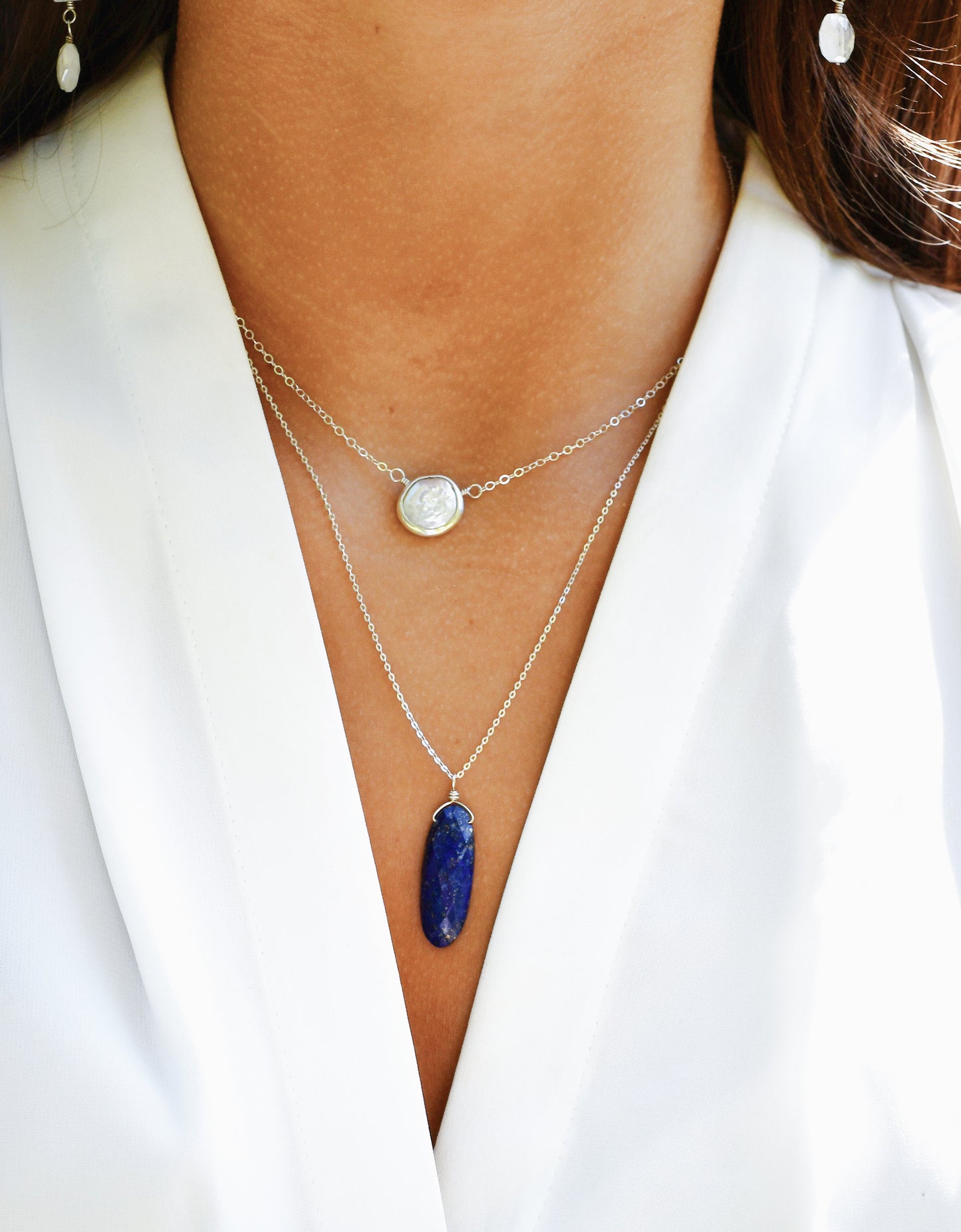 Close-up of a person wearing layered necklaces with a blue lapis lazuli pendant and white freshwater pearl necklace. Handmade jewelry in Connecticut.