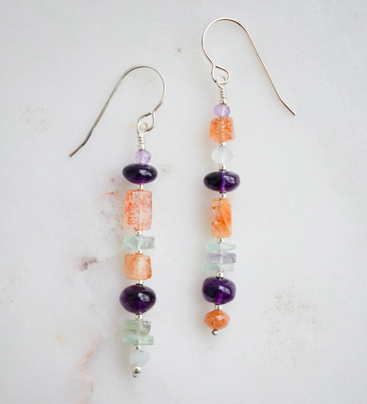 Mismatched gemstone long bar earrings shown in sterling silver. Stones include: amethyst, aquamarine, fluorite, and sunstone. Stones are set onto a long straight bar.