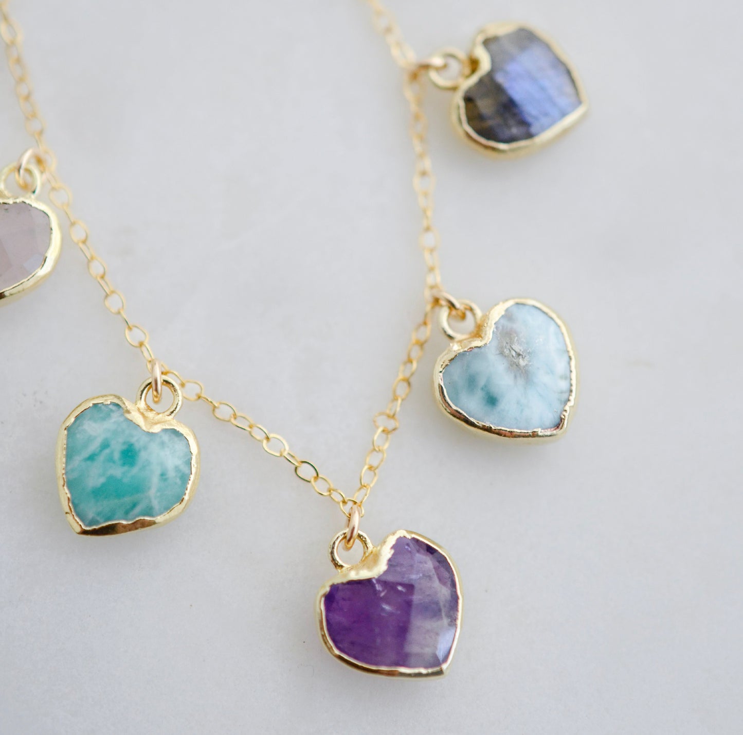 Close up image: Handmade dainty heart necklace with heart-shaped gemstones on a 14k gold filed chain. Stones include: Aquamarine, Rose Quartz, Amazonite, Larimar, Labradorite, Amethyst, and Rainbow Moonstone