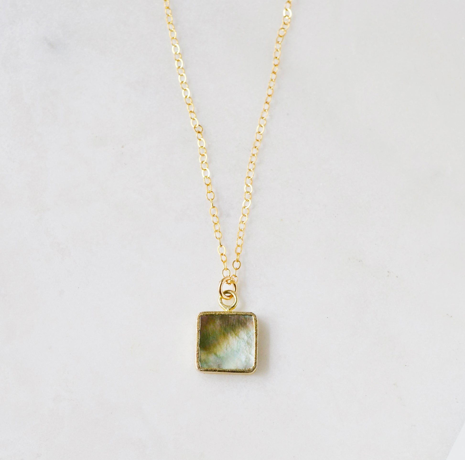 A natural silver colored mother of pearl square shaped pendant set on a 14k gold filled chain. This necklace is handmade in Connecticut by Gemnia.