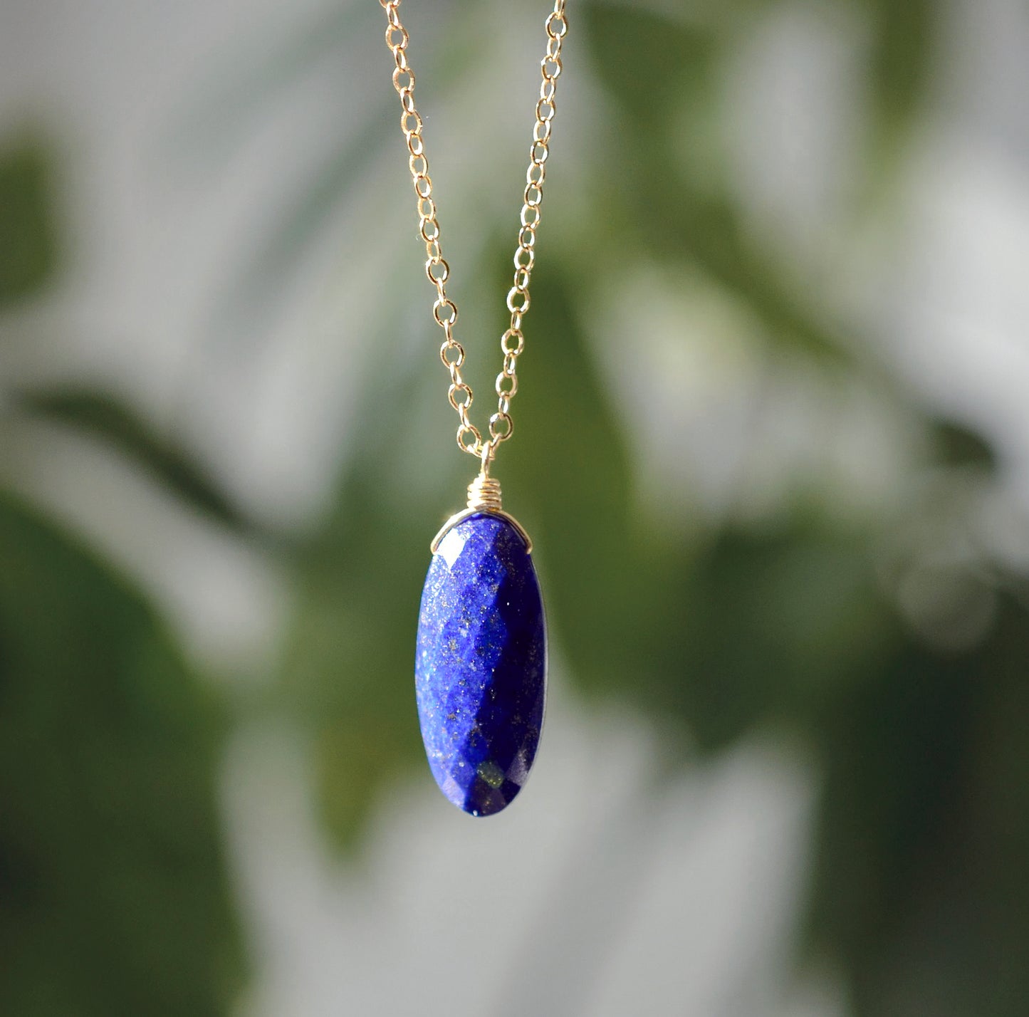 A genuine natural blue Lapis Lazuli faceted oval stone pendant hangs from a 14k gold filled chain. This necklace is handmade in Connecticut by Gemnia Jewelry.
