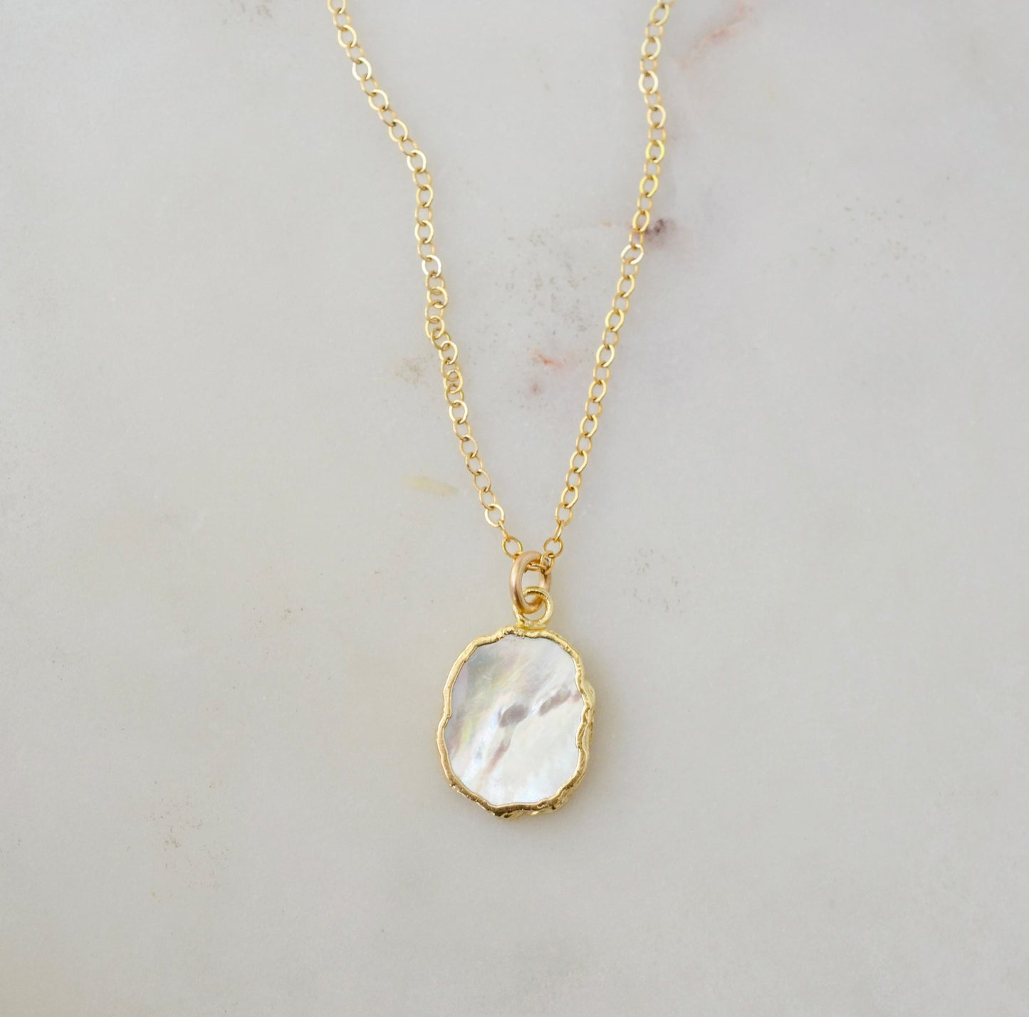 A smooth polished natural, white mother of pearl slice has been set in a 24k gold electroplated bezel and suspended from a 14k gold filled chain. The shell shimmers in shades of white, silver, and pink.