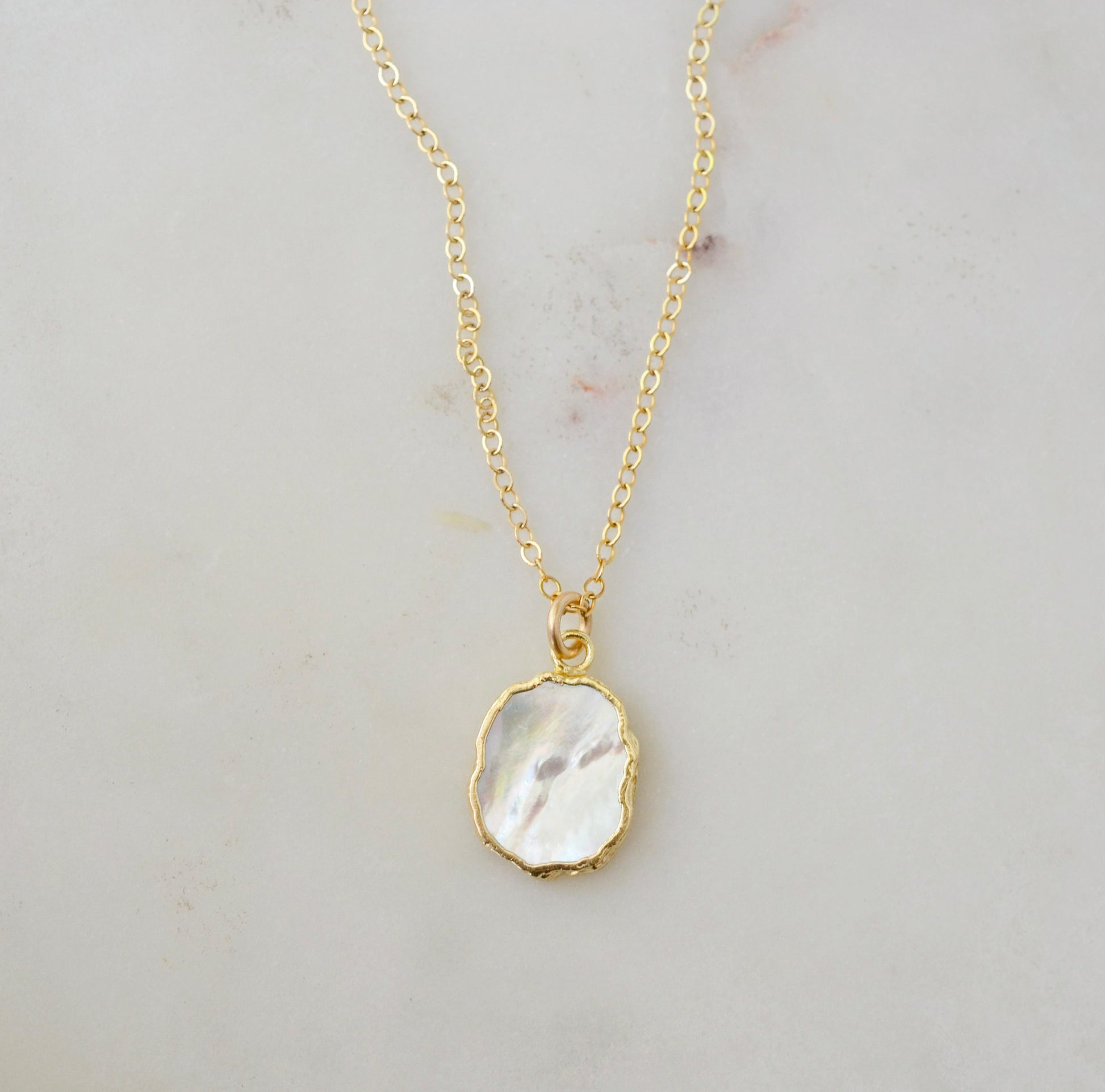 A smooth polished natural, white mother of pearl slice has been set in a 24k gold electroplated bezel and suspended from a 14k gold filled chain. The shell shimmers in shades of white, silver, and pink.