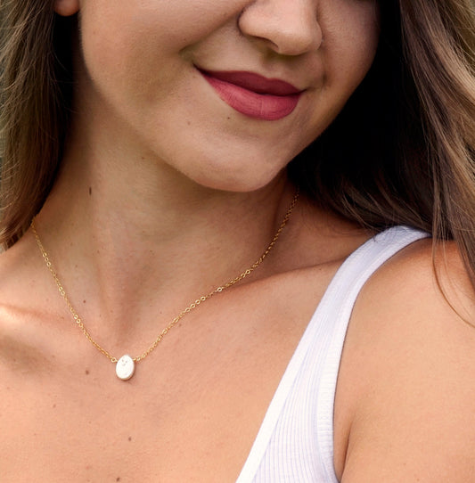 Single white oval shaped freshwater pearl suspended from a sterling silver or 14k gold filled cable chain. Modeled image.