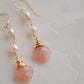 Two white semi-round pearls hang over natural peach Moonstone faceted drops. The gold style is shown.