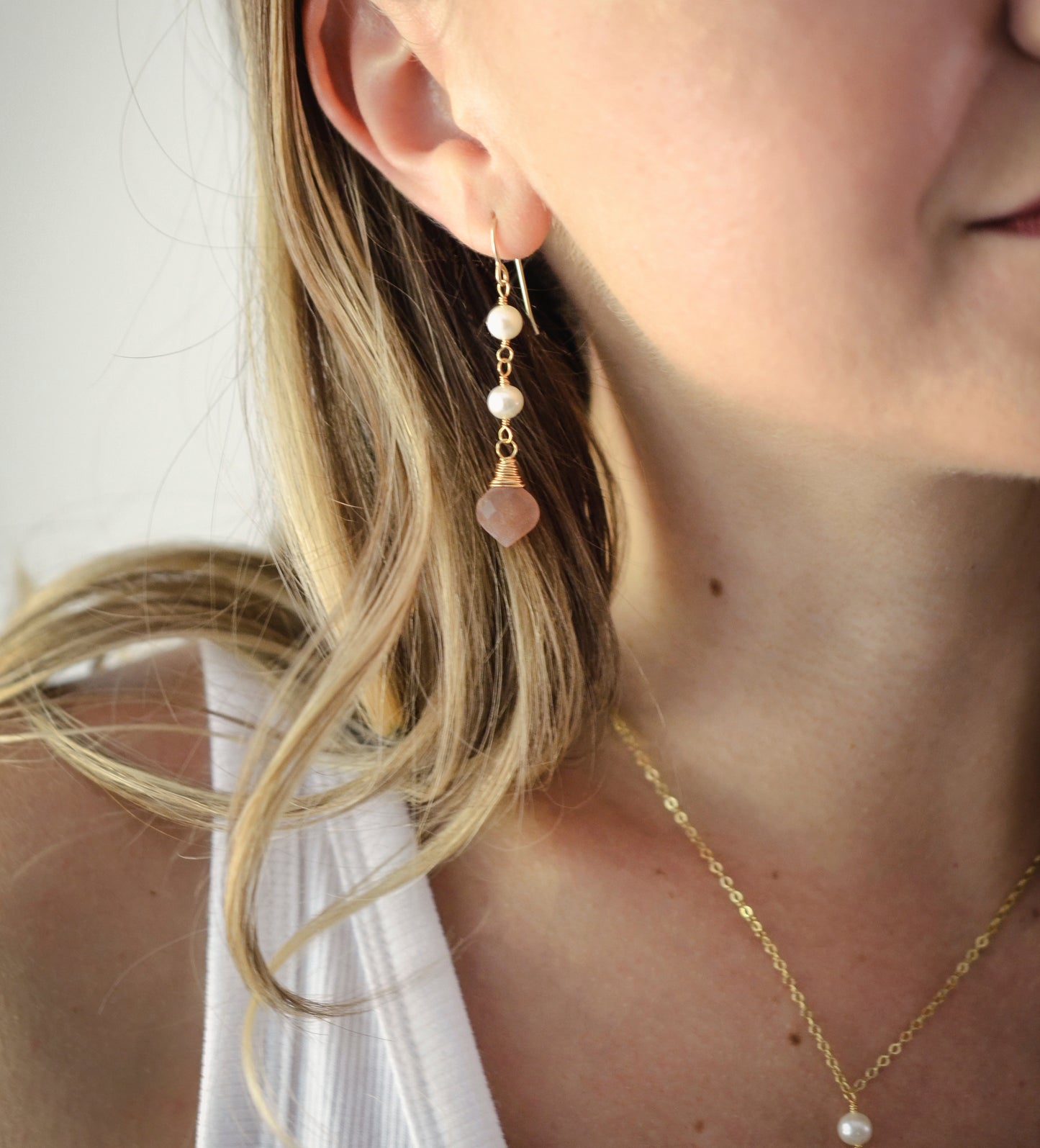 Two white semi-round pearls hang over a natural peach Moonstone faceted drop. The gold style pendant is shown.