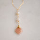 Two white semi-round pearls hang over a natural peach Moonstone faceted drop. The gold style pendant is shown.