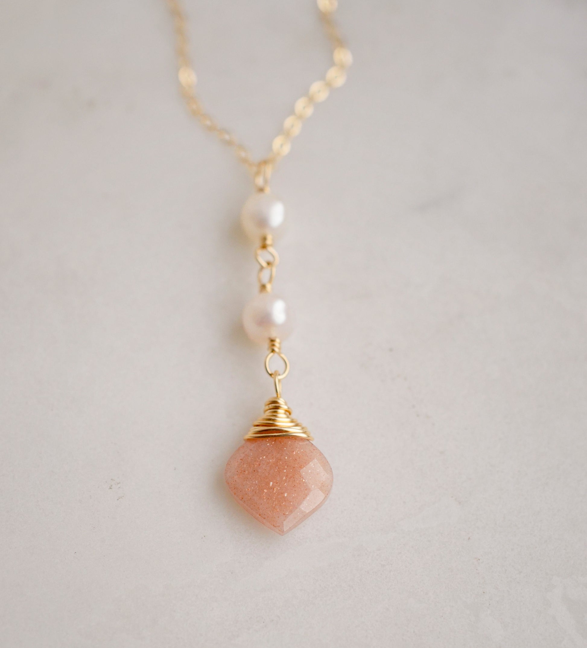 Two white semi-round pearls hang over a natural peach Moonstone faceted drop. The gold style pendant is shown.