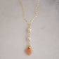 Two white semi-round pearls hang over a natural peach Moonstone faceted drop. The gold style pendant is shown.