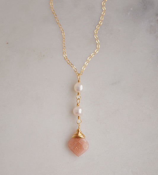 Two white semi-round pearls hang over a natural peach Moonstone faceted drop. The gold style pendant is shown.